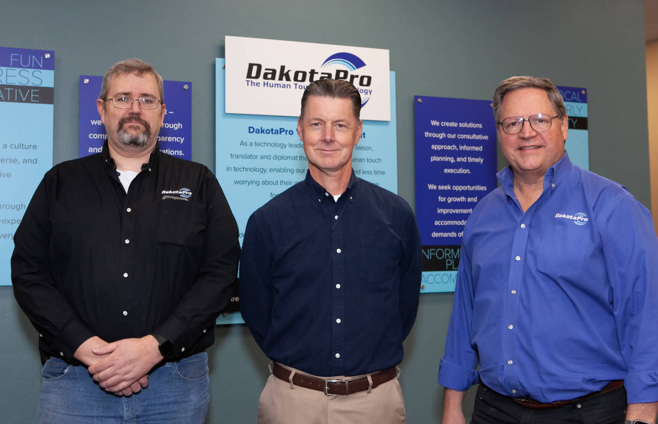 3 male technical support specialist standing in front of a wall containing information about DakotaPro