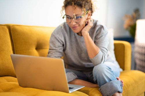 A woman with curly hair sitting on a yellow couch using a computer maybe with slow internet
